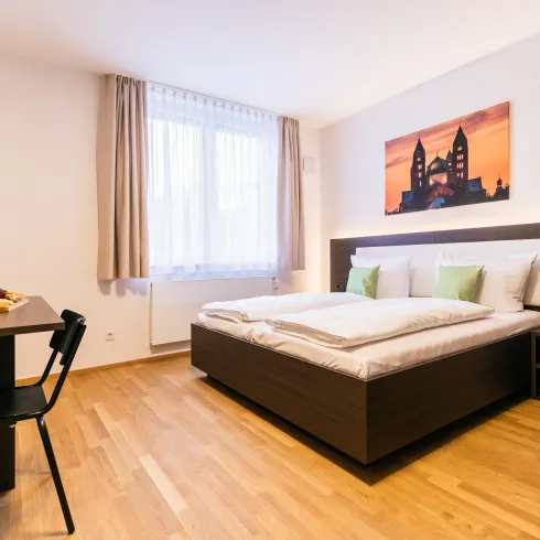 Ein gemütliches Schlafzimmer mit einem großen Bett und Holzboden. Neben dem Bett steht ein Tisch mit Snacks und Wein, sowie ein Fernseher an der Wand.