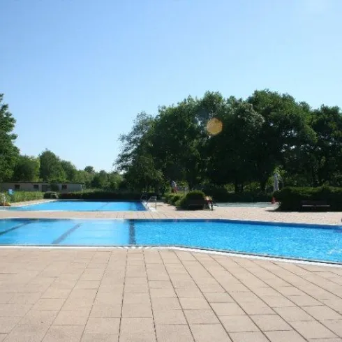 Ein klarer Pool mit zwei Schwimmbecken und einer Rutsche. Umgeben von Bäumen und einer hellen, sonnigen Atmosphäre.