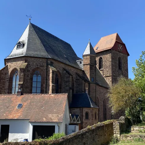 Eine alte Kirche mit zwei Türmen und einem roten Dach. Bäume und ein blauer Himmel umgeben die Szene.