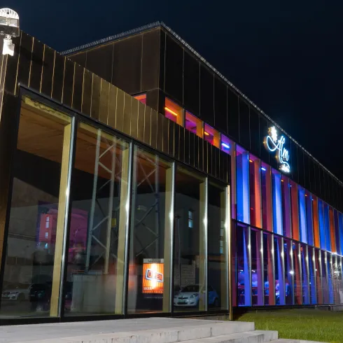 Ein modernes Gebäude mit einer auffälligen Fassade aus Glas und Metall. Es ist nachts beleuchtet und zeigt bunte Lichter.