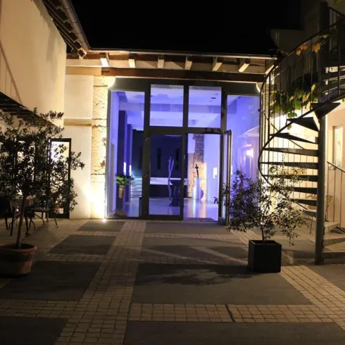 Ein einladender Innenhof mit modernen Elementen, der von Pflanzen umgeben ist. Im Hintergrund leuchtet ein blauer Raum, der eine angenehme Atmosphäre schafft.