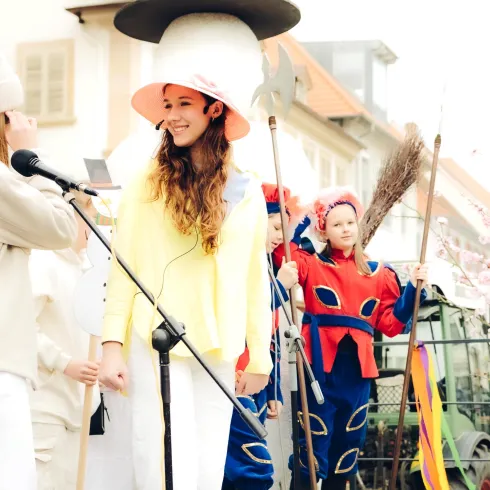 Eine fröhliche Faschingsfeier mit Menschen in bunten Kostümen. Im Vordergrund stehen zwei Frauen, die miteinander sprechen und eine bunte Atmosphäre schaffen.