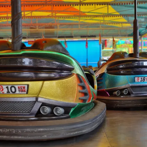 Bumper Cars auf einem Jahrmarkt unter einem bunten Zelt. Die Fahrzeuge haben auffällige Farben und Nummernschilder.