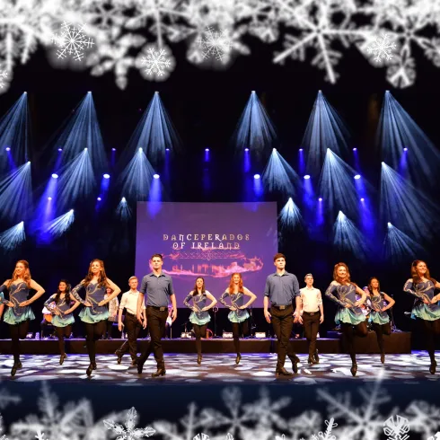 Eine Tanzaufführung auf der Bühne mit mehreren Tänzern in bunten Kostümen. Der Hintergrund ist mit bunten Lichtern und einem großen Banner dekoriert.