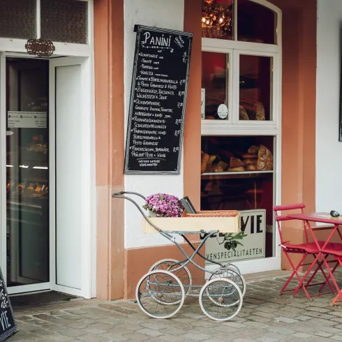Ein gemütliches Café mit Tischen und Stühlen im Freien. Die Wände sind mit Tafeln beschriftet, die die Speisen und Getränke auflisten.