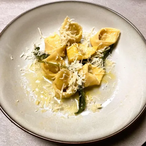 Ein Teller mit frischen Tortellini, garniert mit Käse und grünen Blättern. Die Pasta schwimmt in einer leichten Soße.