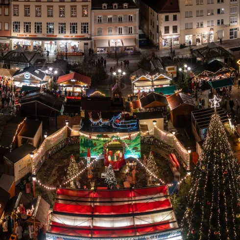Ein festlicher Weihnachtsmarkt mit vielen bunten Ständen und geschmückten Bäumen. Die Atmosphäre ist lebhaft und einladend, voller Lichter und Menschen.