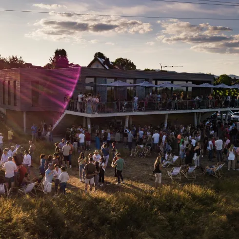 Eine große Menschenmenge versammelt sich vor einem Gebäude bei Sonnenuntergang. Die Atmosphäre ist festlich und einladend.