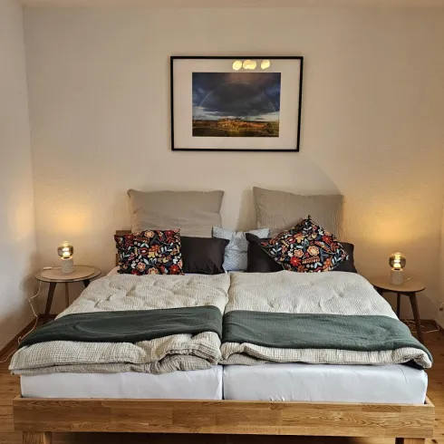 Ein gemütliches Schlafzimmer mit einem Doppelbett und bunten Kissen. Sanftes Licht von den Nachttischlampen schafft eine einladende Atmosphäre.