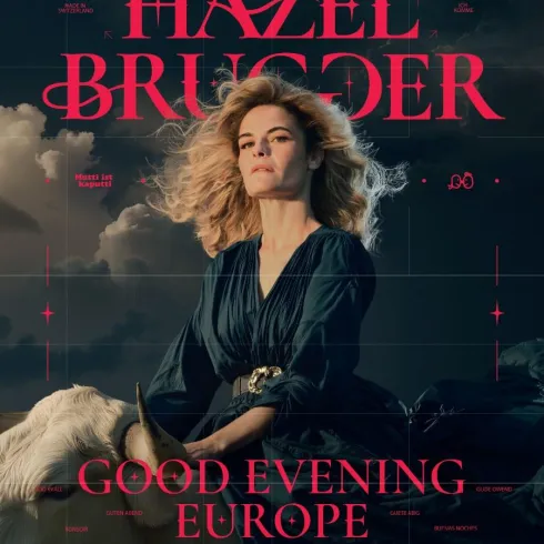 Ein Porträt einer Frau mit blonden Locken, die in einem eleganten schwarzen Kleid posiert. Im Hintergrund steht ein weißes Pferd und der Text „GOOD EVENING EUROPE“ ist sichtbar.