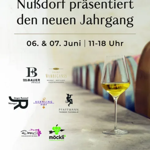 Ein elegantes Weinglas mit einem hellen Getränk steht auf einem Tisch. Im Hintergrund sind gemütliche Sitzgelegenheiten und eine Ankündigung für eine Weinpräsentation zu sehen.