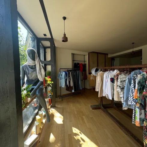 Ein moderner Bekleidungsladen mit einer hellen und einladenden Atmosphäre. Kleidung hängt ordentlich auf Ständern und es gibt eine ansprechende Dekoration am Fenster.