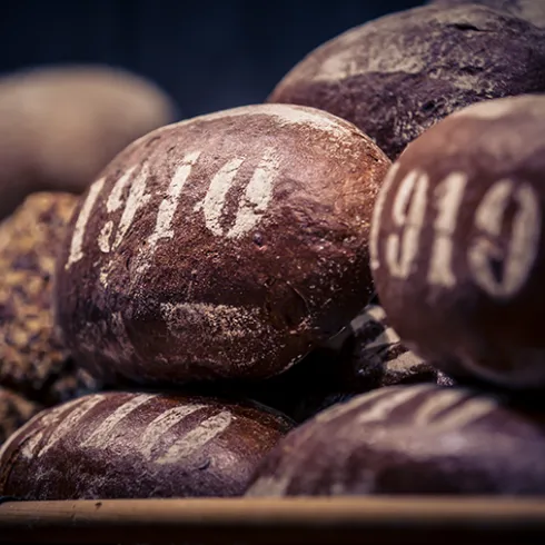 Eine Ansammlung von braunen Broten mit der Jahreszahl 1910 auf der Oberfläche. Die Brote sind unregelmäßig geformt und wirken frisch gebacken.