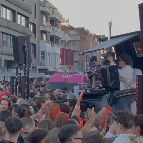 Eine große Menschenmenge feiert auf einer Straße, während DJs Musik spielen. Die Atmosphäre ist lebhaft und energiegeladen.