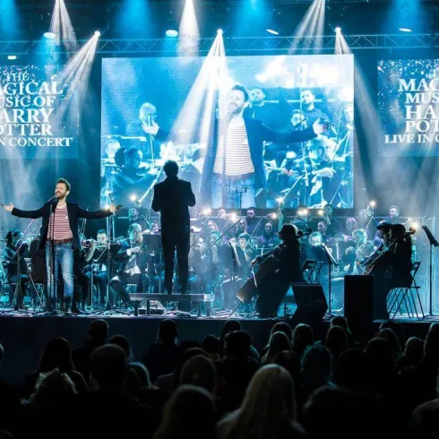 Ein Live-Konzert mit einem Sänger und einem Orchester. Das Licht erleuchtet die Bühne, während die Musik aus Harry Potter gespielt wird.