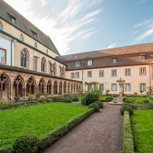Ein ruhiger Innenhof mit grünen Rasenflächen und schön gestalteten Hecken. Historische Gebäude umgeben den Innenraum und der Himmel ist teilweise bewölkt.