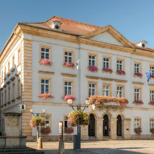 Ein historisches Gebäude mit blühenden Blumenkästen an den Fenstern. Der klare Himmel und die schöne Architektur verleihen der Szene eine einladende Atmosphäre.