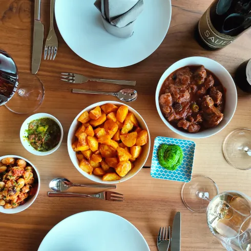 Ein festlich gedeckter Tisch mit verschiedenen Gerichten. Es gibt Gnocchi, Fleischgerichte und mehrere Weingläser.