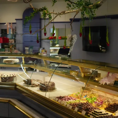 Eine elegante Konditorei mit einer Auswahl an köstlichen Kuchen und Süßigkeiten. Die Theke ist reich dekoriert und lädt zum Probieren ein.