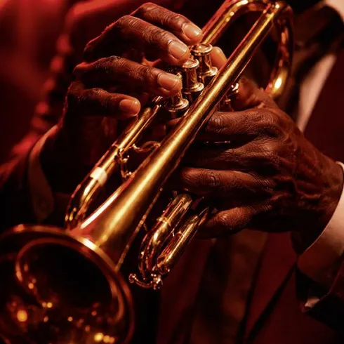 Ein Musiker spielt eine goldene Trompete in einem stimmungsvollen, rötlichen Licht. Die Hände zeigen die Detailtreue und Leidenschaft des Spiels.
