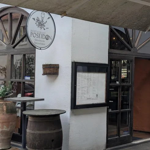 Das Bild zeigt den Eingang eines Restaurants mit dem Namen "Poseidon". Es hat große Fenster und eine einladende Atmosphäre.