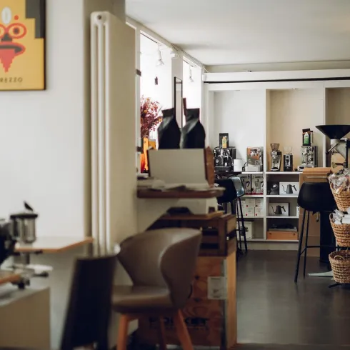 Ein modernes Café mit einer einladenden Atmosphäre. Es gibt Tische, Stühle und dekorative Elemente an den Wänden.