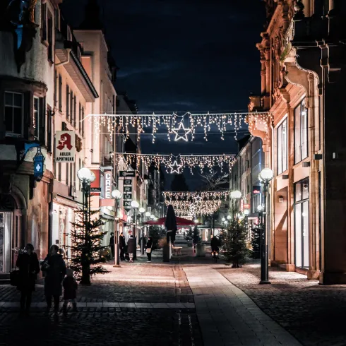Eine festlich beleuchtete Straße bei Nacht mit Weihnachtslichtern und dekorierten Tannenbäumen. Die Atmosphäre ist gemütlich und einladend.