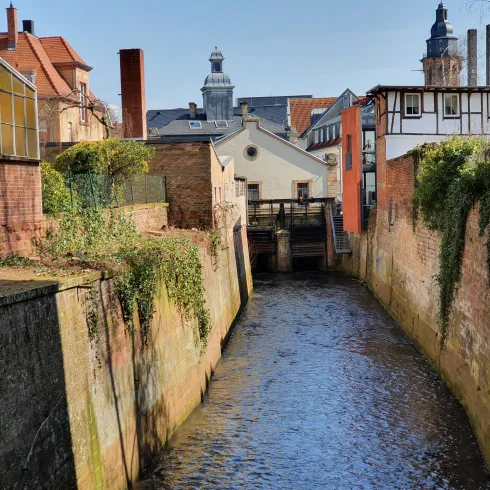Eine ruhige Wasserstraße zwischen alten Backsteinmauern. Im Hintergrund sind historische Gebäude und ein Kirchturm zu sehen.
