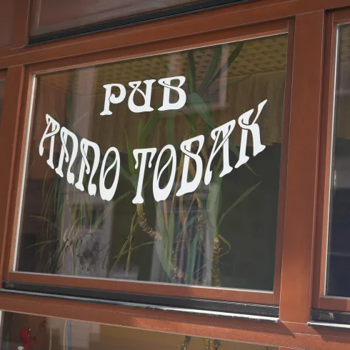 Ein Fenster mit der Aufschrift "Pub Anno Tobak". Die Schrift ist auffällig und befindet sich in einem Holzrahmen.