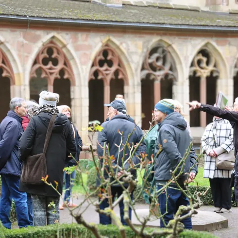 Eine Gruppe von Menschen steht in einem Innenhof eines Klosters. Sie scheinen einer Führung zu folgen und diskutieren miteinander.