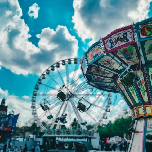 Ein bunter Jahrmarkt mit einem Riesenrad und einem Schwingkarussell. Der Himmel ist klar und mit vielen schönen Wolken übersät.