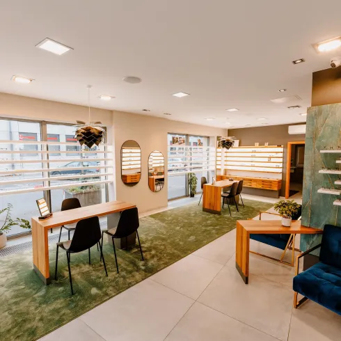 Ein modernes, helles Innenraum mit Holz- und grünen Akzenten. Es gibt elegante Möbel, Pflanzen und große Fenster, die für eine angenehme Atmosphäre sorgen.