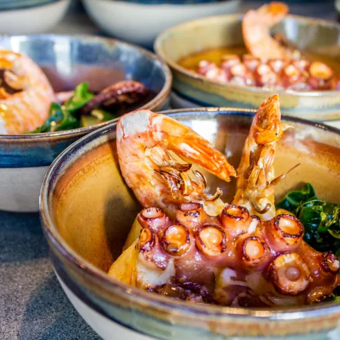 Eine Schüssel mit Garnelen und Oktopus, umgeben von frischem Gemüse. Die Farben der Speisen sind lebhaft und appetitlich.