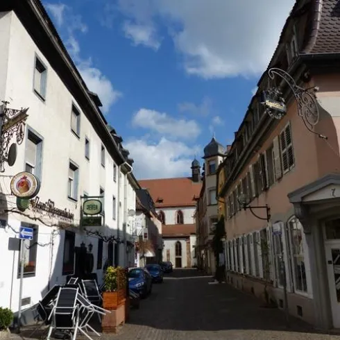 Eine malerische Straßenansicht mit alten Gebäuden und einladenden Cafés. Der Himmel ist klar und blau, was die charmante Atmosphäre unterstreicht.