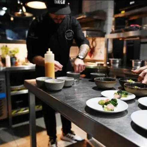 In einer modernen Küche bereiten Köche verschiedene Gerichte vor. Auf dem Tisch stehen mehrere Schalen und Teller mit sorgfältig angerichteten Speisen.