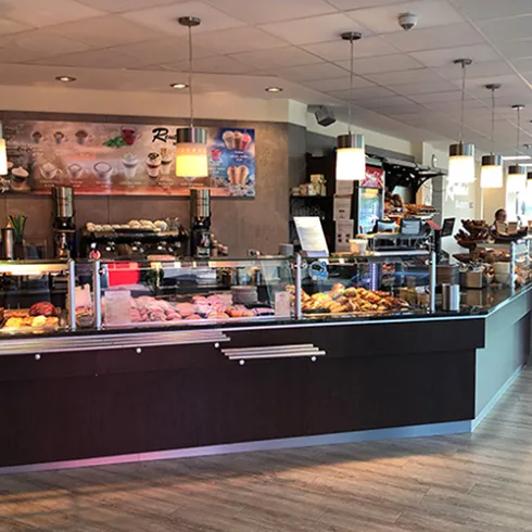 Ein einladendes Café mit einer Theke, die verschiedene Backwaren und Desserts präsentiert. Die Atmosphäre ist hell und freundlich, ideal für entspannte Stunden.