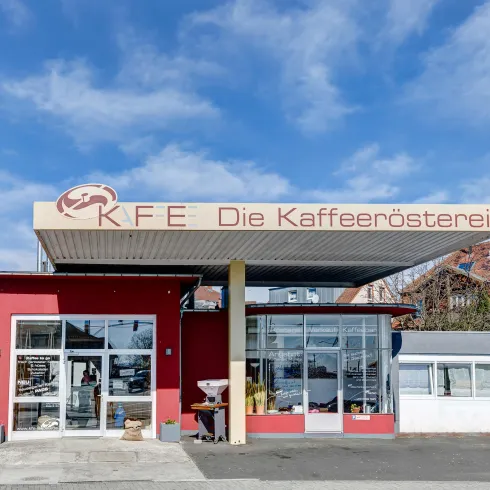 Ein hübsches Kaffeehaus mit einem modernen Design. Die Fassade ist rot und hat große Fenster, die einen einladenden Blick auf den Innenraum bieten.