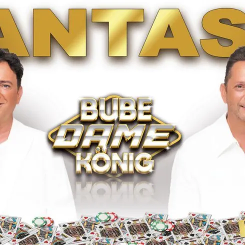 Zwei Sänger in weißen Anzügen lächeln freundlich in die Kamera. Im Hintergrund steht der Schriftzug "FANTASY" und weitere Details zu einer Veranstaltung.