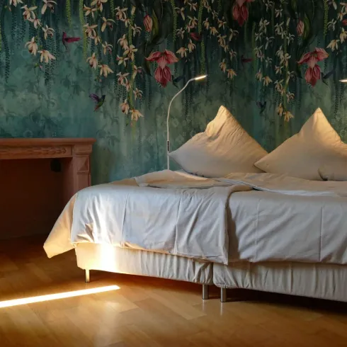 Ein helles Schlafzimmer mit einem großen Bett und zwei Kissen. Die Wände sind mit einer schönen Blumenmalerei dekoriert.