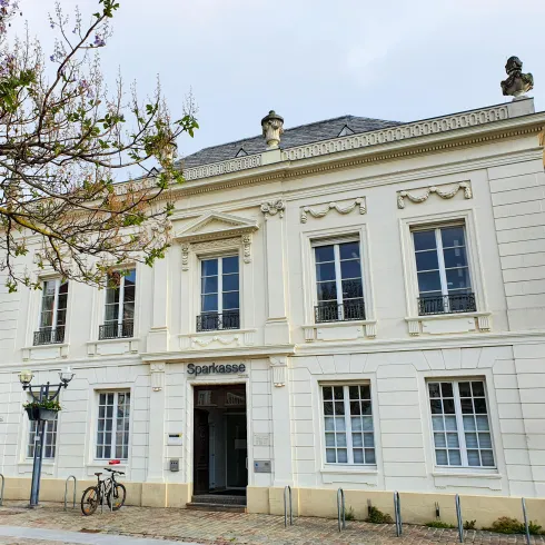 Ein elegantes Gebäude mit einer weißen Fassade und großen Fenstern. Darauf steht "Sparkasse" in moderner Schrift.