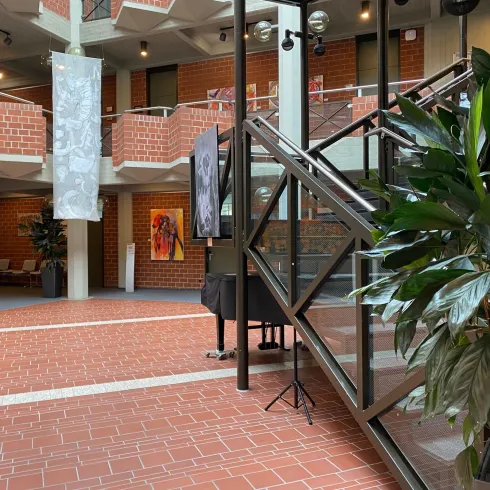 Ein moderner Innenraum mit roten Ziegelwänden und einer Treppe aus Glas. Im Hintergrund sind Pflanzen und Kunstwerke zu sehen.