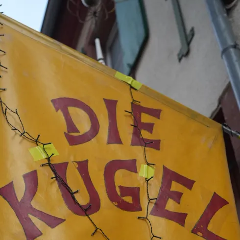 Ein großes, gelbes Schild mit der Aufschrift "DIE KUGEL". Es enthält auch eine Webadresse am unteren Rand.