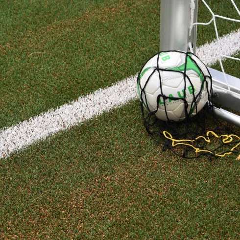 Ein Fußball liegt in der Ecke eines Fußballtors auf dem Spielfeld. Das Netz ist teilweise um den Ball gewickelt.