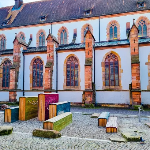 Ein historisches Gebäude mit bunten Holzstrukturen im Vordergrund. Die schönen Fenster und die Architektur verleihen dem Ort Charme.