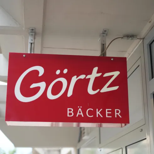 Ein rotes Schild mit der Aufschrift "Görtz Bäcker". Es zeigt den Eingang einer Bäckerei.