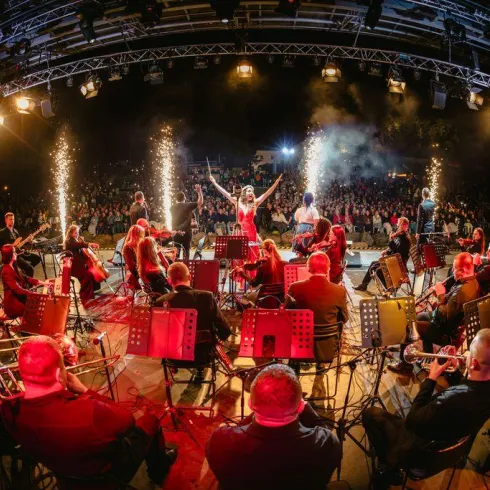 Ein lebhaftes Konzert mit einem großen Orchester auf der Bühne. Funkelnde Feuerwerkskörper sorgen für eine festliche Atmosphäre.