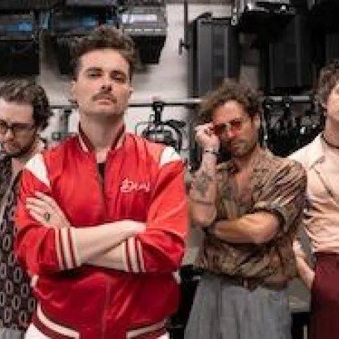Vier Männer stehen mit unterschiedlichen Posen und coolen Outfits vor einer Kulisse von Lichttechnik. Sie wirken kreativ und stylisch.