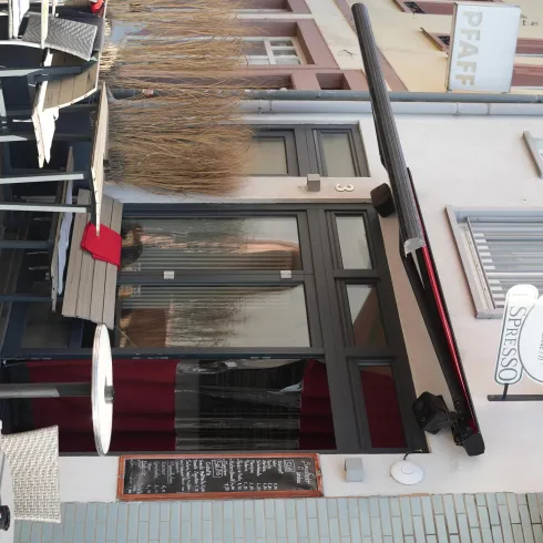 Ein kleines Bistro mit einer einladenden Eingangstür und Stühlen draußen. Die Atmosphäre ist gemütlich und einladend.