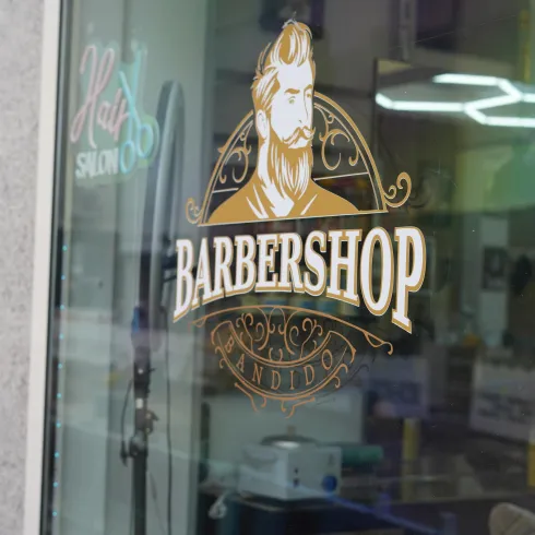 Ein Schaufenster eines Barbierladens mit einem stilvollen Logo. Das Logo zeigt einen bärtigen Mann und den Schriftzug "BARBERSHOP".