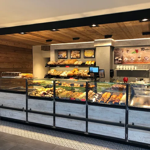 Eine moderne Bäckerei mit einem ansprechend gestalteten Verkaufsbereich. Es sind verschiedene frisch gebackene Brötchen und Gebäcksorten ausgestellt.